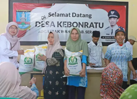 Kabid Ketahanan Pangan DKPP Kabupaten Serang, Mumun Munawaroh (kiri), simbolis menyerahkan bantuan pangan beras kepada KPM di kantor Desa Kebon Ratu, Rabu, 30 Juli 2025. (Sumber: Dok Kominfo Pemkab Serang)