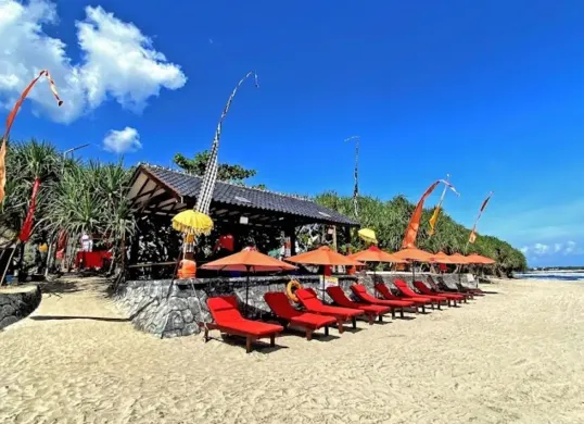 Deretan kursi panjang berwarna merah dengan payung oranye berjajar rapi di atas pasir Pantai Karang Papak, Garut. Nuansa Bali semakin terasa dengan hiasan kain poleng dan umbul-umbul di sekitar area. (Sumber: Villa&Cafe Villa Rahayu Karangpapak)