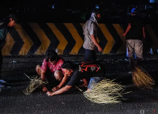 Sejumlah warga menggunakan sapu untuk mengambil uang sedekah yang dilempar para pengendara mudik di Jalur Pantura Sukra, Indramayu, Jawa Barat, Jumat, 28 Maret 2025. (Sumber: Poskoata/ Bilal Nugraha Ginanjar)
