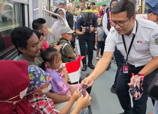 Petugas KRL membagikan bendera merah putih dan sosialisasi memberikan harga Rp8 naik KRL Commuter disambut antusias warga pengguna moda transportasi kereta. (Sumber: KRL Commuter Line)