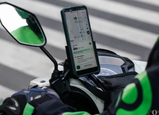 Driver ojol menggunakan ponsel di pinggir jalan saat menunggu orderan, ilustrasi pentingnya perangkat andal di tengah mobilitas tinggi. (Sumber: Poskota/Bilal Nugraha Ginanjar)