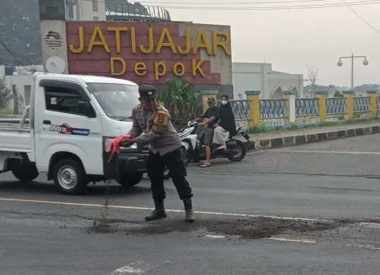 Anggota Polsek Sukmajaya menutupi jalan terkena ceceran oli di Jalan Raya Bogor, Cilodong, Depok (depan terminal Jati Jajar). (Foto: Angga PahIevi)