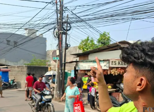 Ketua RT 14 RW 005, Rifki Ramadhan menunjukan lokasi tiang listrik kabel semerawut yang berada di pinggir Jalan Kramat Pulo Dalam. (Sumber: Poskota/Angga)
