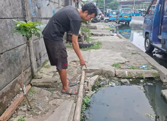 Rahmat, warga RT 07 RW 19 menunjukan luapan air got yang berasal dari lubang gorong-gorong yang terbuka di Jalan Naming Botin Kelurahan Depok, Kecamatan Pancoran Mas, Kota Depok, Selasa siang, 13 Oktober 2026. (Sumber: Poskota/Angga)