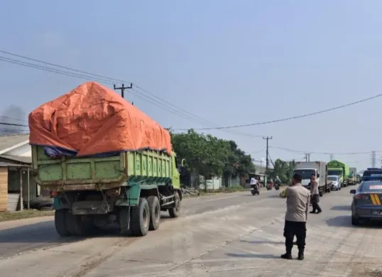 Petugas Polsek Jawilan mengarahkan kendaraan dump truk yang parkir di bahu jalan untuk mengisi kantong-kantong parkir. (Sumber: Polsek Jawilan)