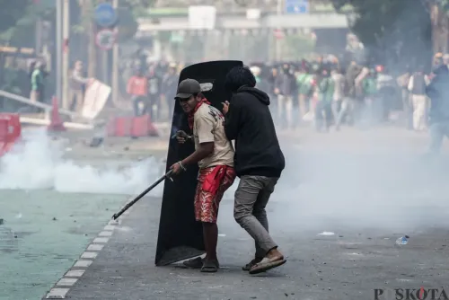 Dua massa aksi berlindung di balik tameng polisi saat demonstrasi di Mako Brimob Polda Metro Jaya, Kecamatan Senen, Jakarta Pusat, Jumat, 29 Agustus 2025. (Sumber: Poskota/Bilal Nugraha Ginanjar)