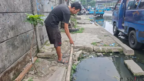 Rahmat, warga RT 07 RW 19 menunjukan luapan air got yang berasal dari lubang gorong-gorong yang terbuka di Jalan Naming Botin Kelurahan Depok, Kecamatan Pancoran Mas, Kota Depok, Selasa siang, 13 Oktober 2026. (Sumber: Poskota/Angga)